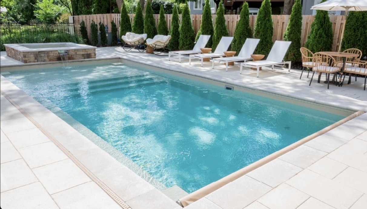 Rectangular fiberglass pool with raised stone spa, light coping, and sun loungers